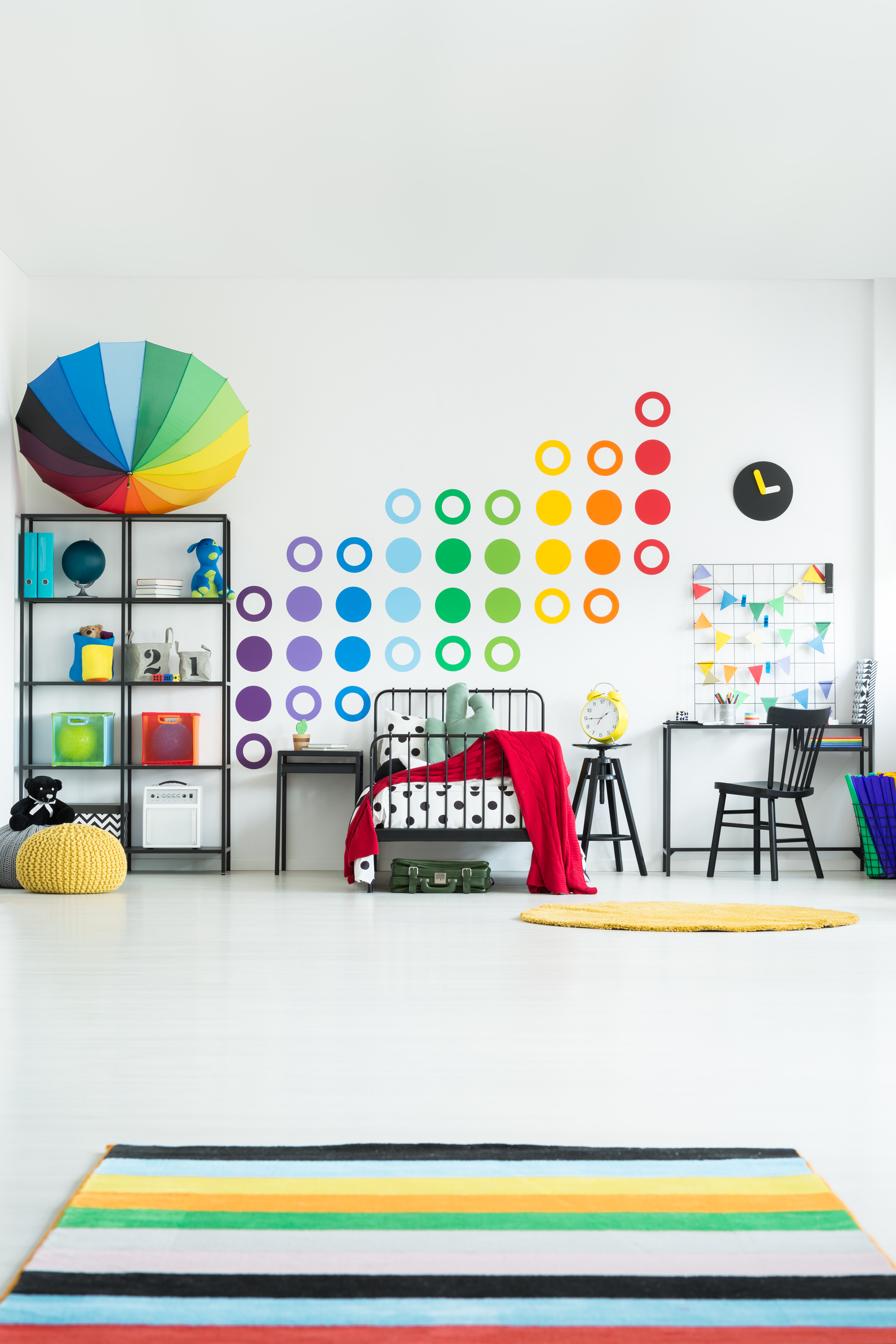 Colorful carpet in scandi child's room with toys and black chair at desk near bed against wall with sticker